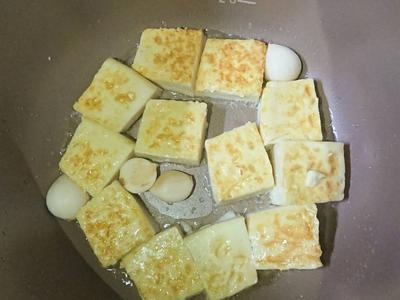 中途約4分鐘時打開鍋蓋將豆腐翻面並加入蒜頭再蓋上鍋蓋（可以使用木製的鍋鏟或飯匙來翻面）